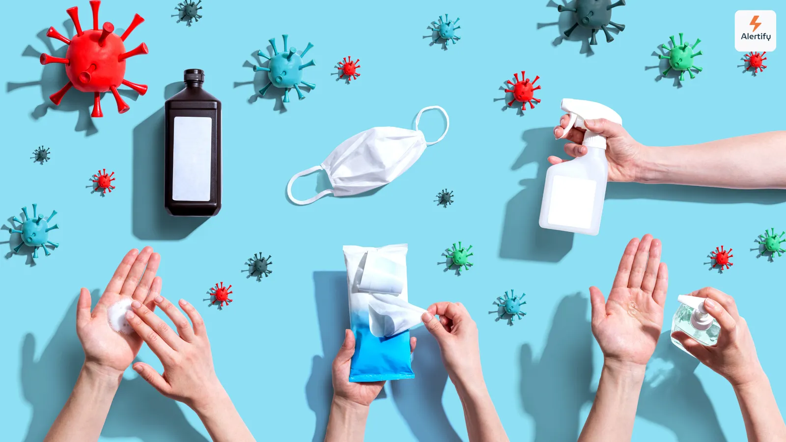 Bovenaanzicht van virusmodellen, een mondkapje, desinfectiespray en handen die hygiëneproducten gebruiken