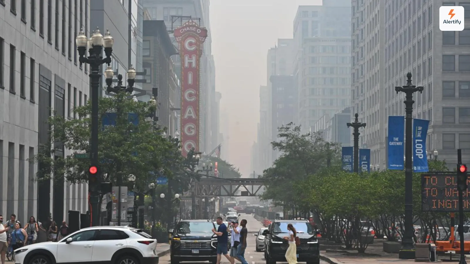 Rook van bosbranden die de gebouwen langs een straat in Chicago aan het zicht onttrekt, met het verlichte bord van het Chicago Theatre op de voorgrond.