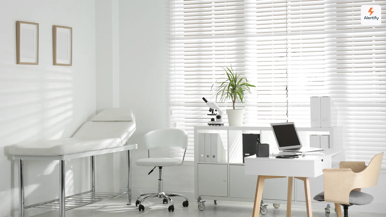Lege spreekkamer met een onderzoeksbank, een bureau met een laptop en jaloezieën voor het raam