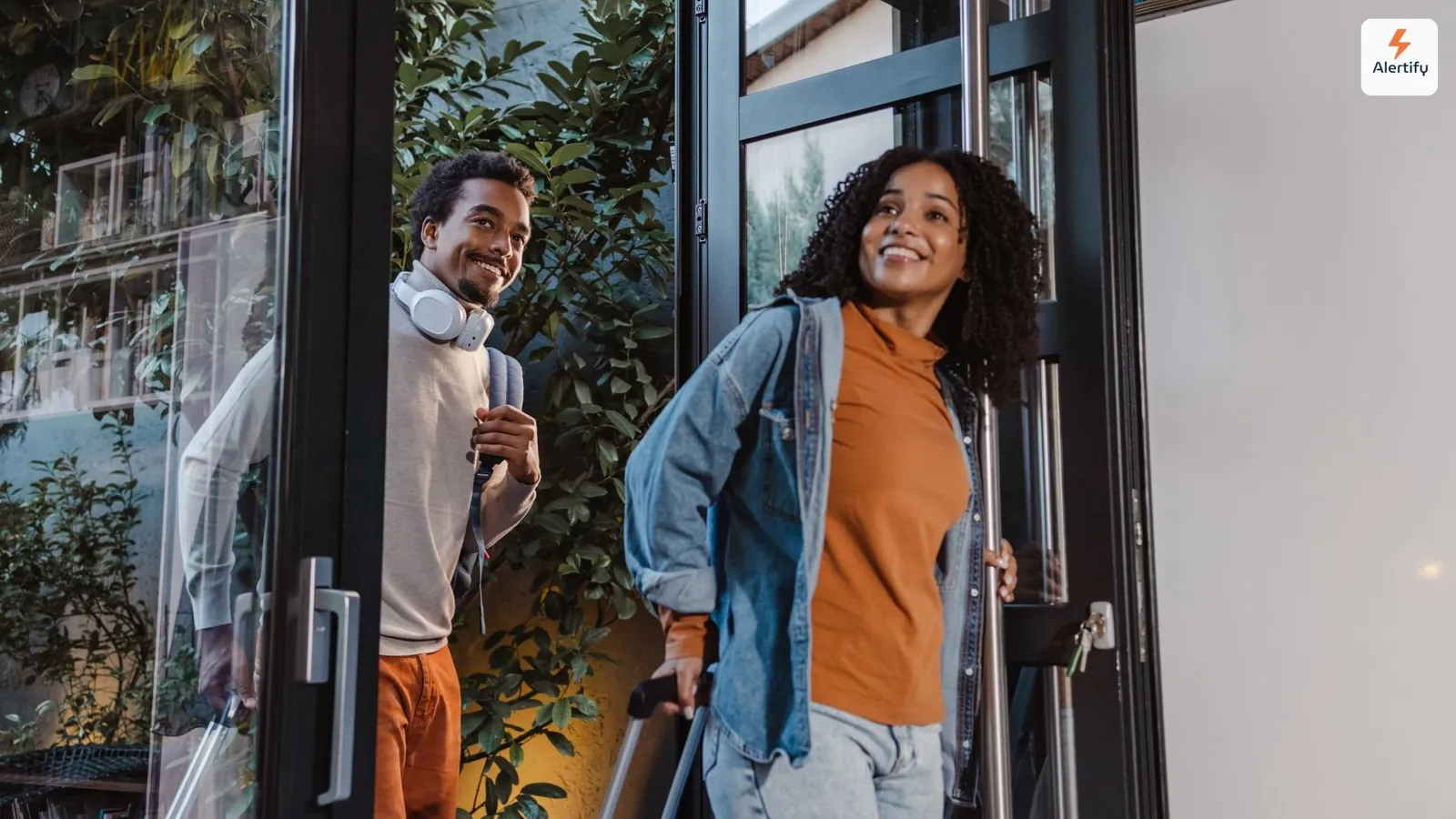 Twee gasten die met rolkoffers bij een verhuurwoning aankomen, lachend terwijl ze door een glazen deur naar binnen komen.