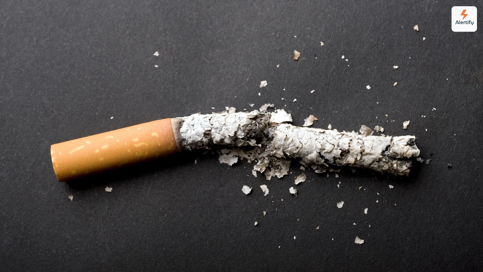 Gebroken sigaret in tweeën met as verspreid over een donker oppervlak