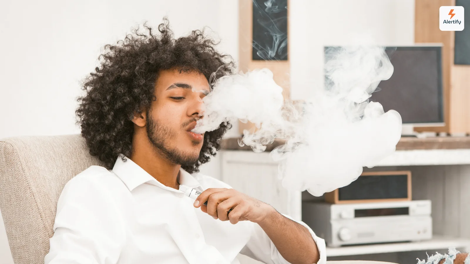 Gast blaast een dikke wolk damp uit terwijl hij in de woonkamer van een vakantiewoning zit