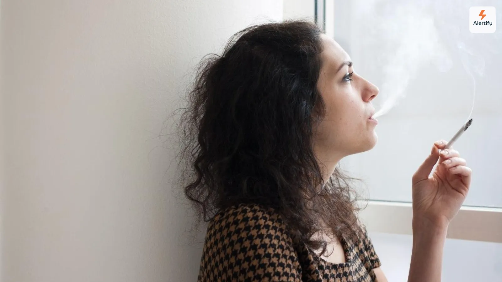 Gast die tegen een muur leunt en binnen een sigaret rookt naast een licht raam in een vakantiewoning